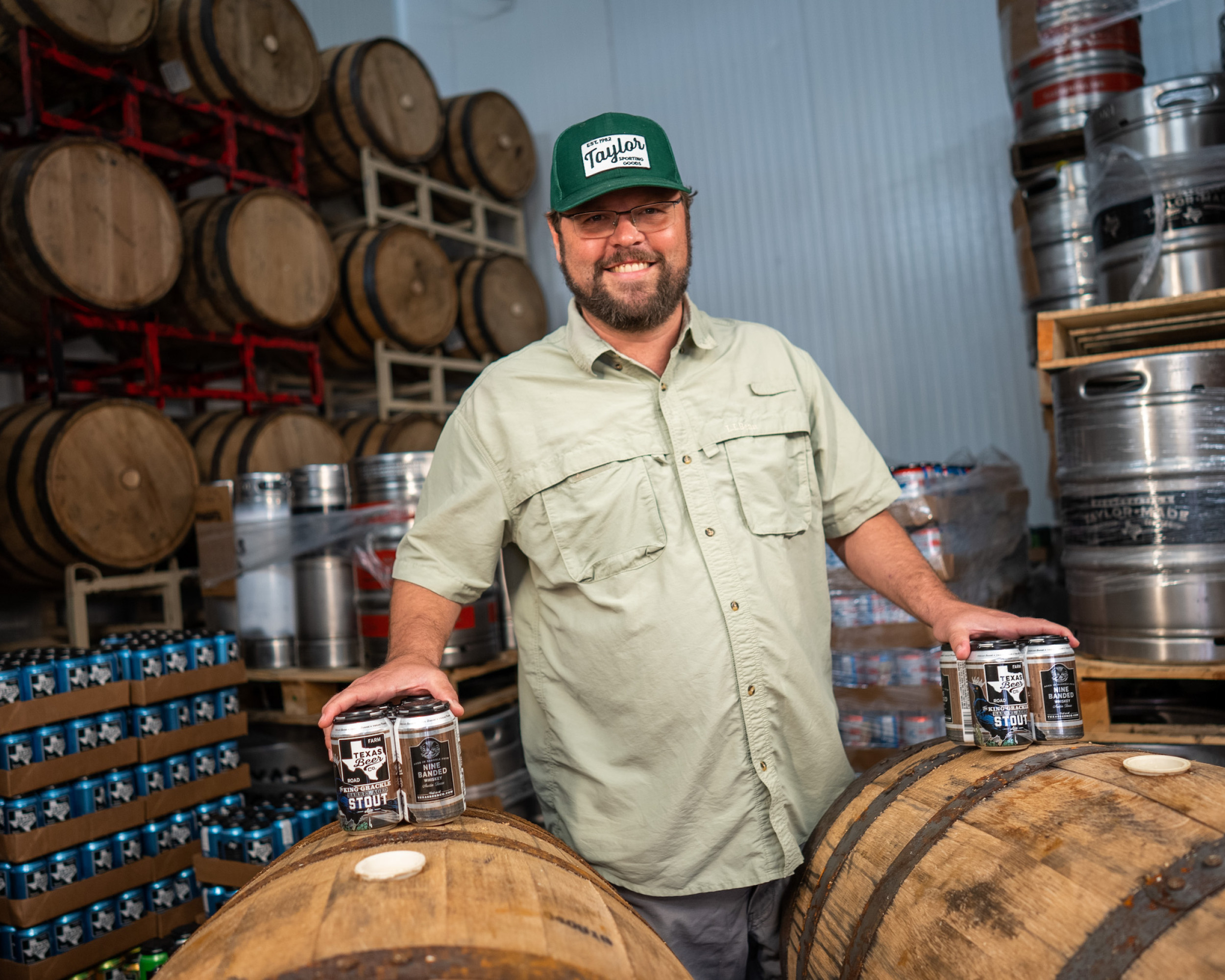 Taylor Beer co owner posing with some of his beer in front of some barrels
